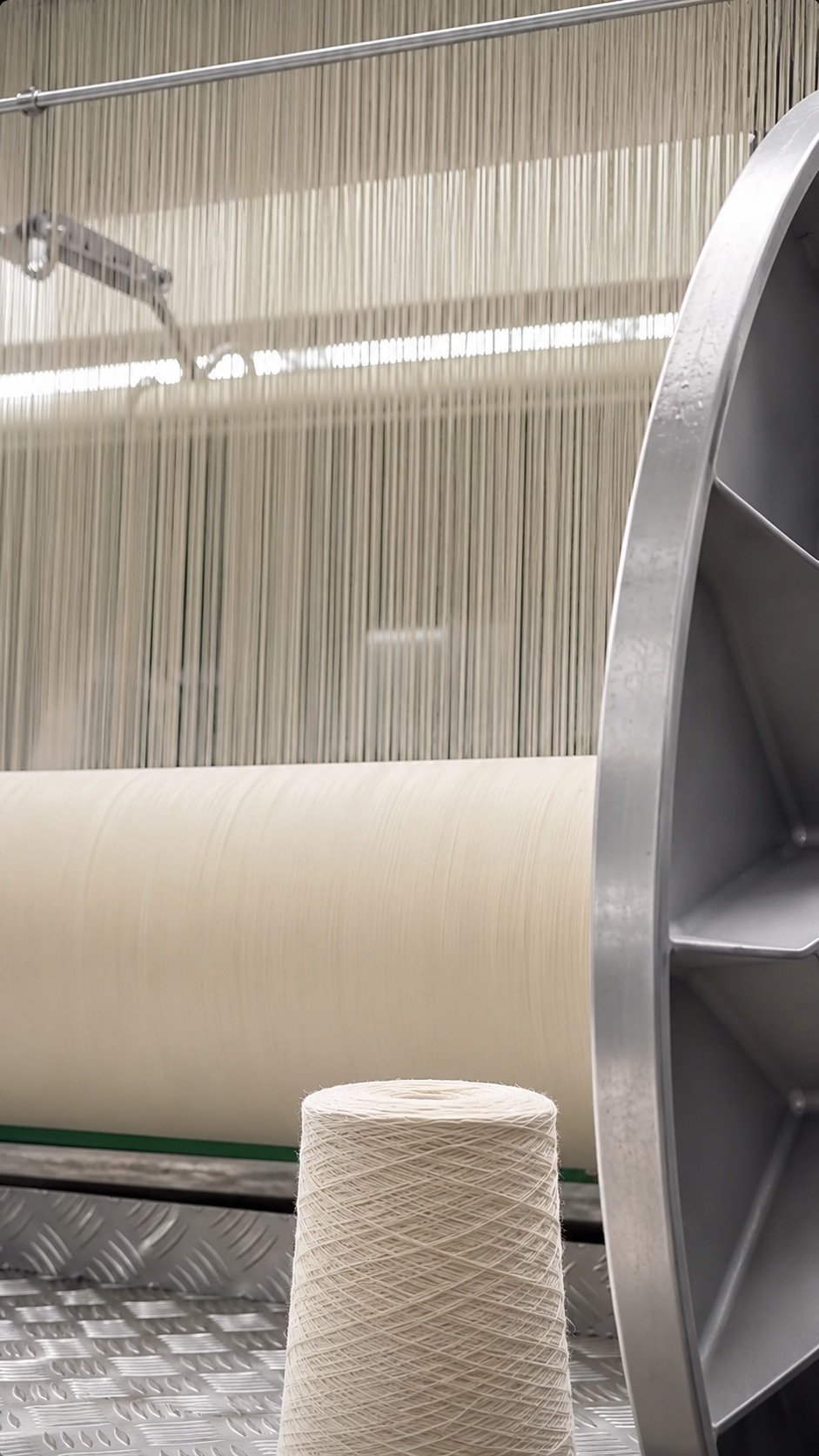 Warp threads running through a loom beside a wound fabric beam and a cone of yarn at Marah Fashion Group